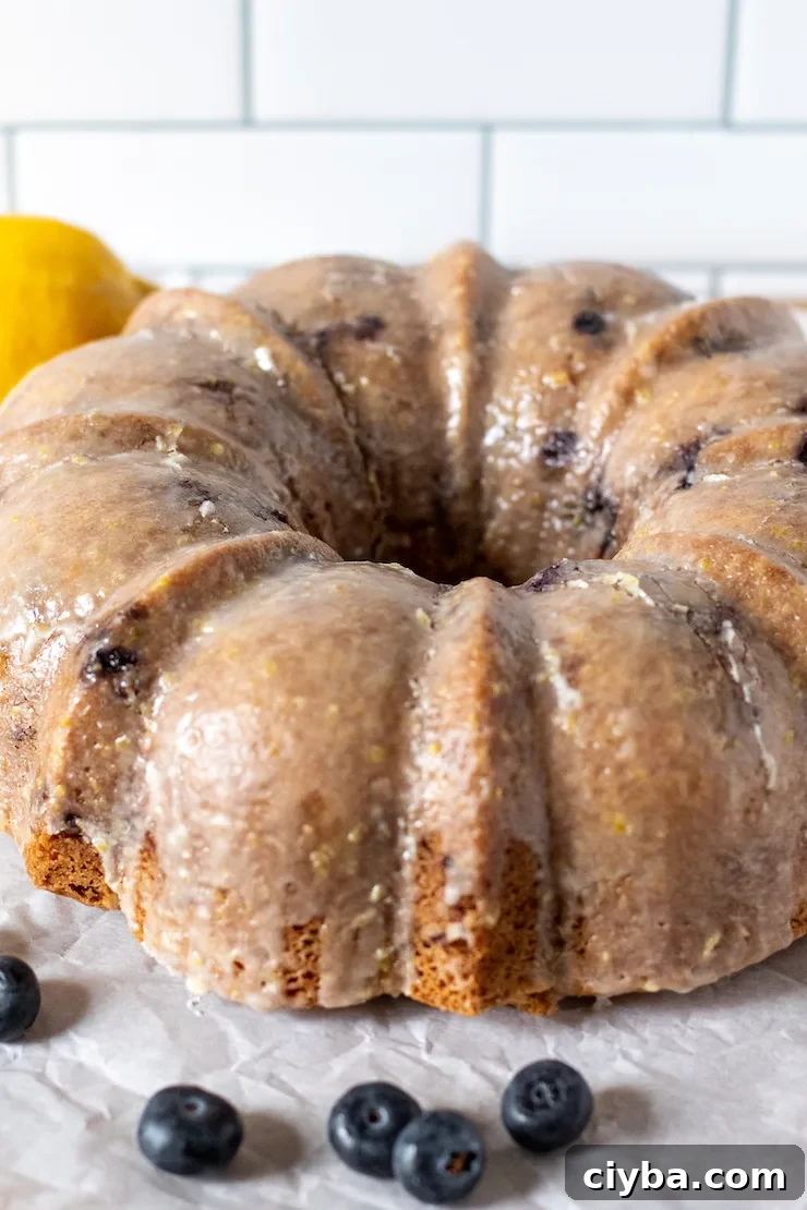Glazed blueberry lemon cake with blueberries and lemon in background.