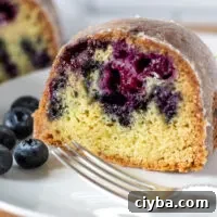Close up of slice of cake on plate with fork and blueberries.