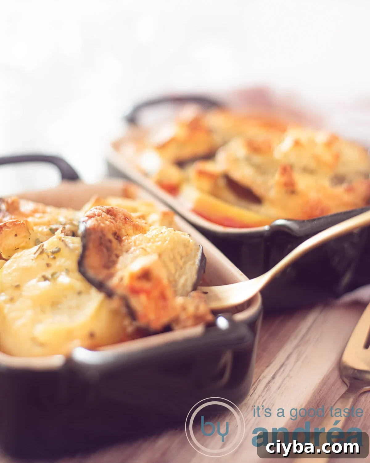 Two one-person Greek moussaka casserole dishes on a wooden board. A golden spoon takes out a scoop.