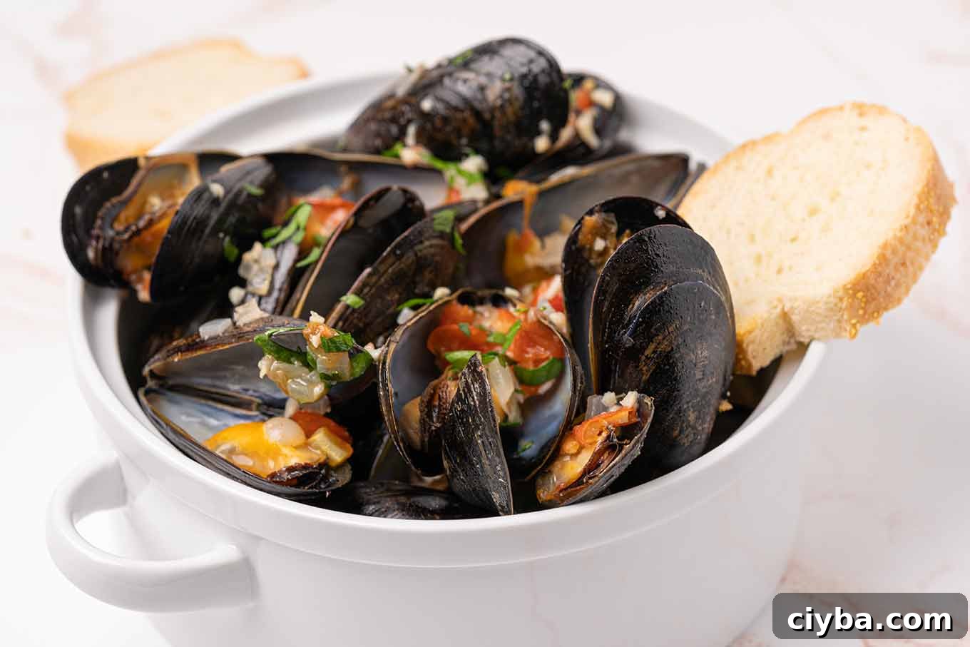 Italian-Style Steamed Mussels with Garlic, White Wine, and Herbs 4 A serving bowl filled with steamed mussels topped with bits of garlic, onion, tomato, and parsley and crusty bread for dipping.