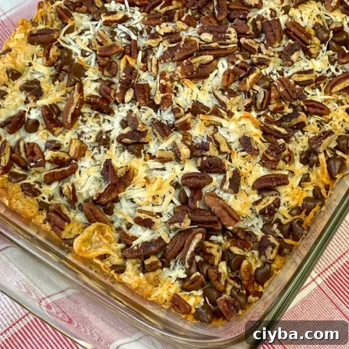 Corner of glass pan on red plaid napkin of the best magic bars with pecans, coconut, chocolate chips, butterscotch chips and sweetened condensed milk on a graham cracker crust