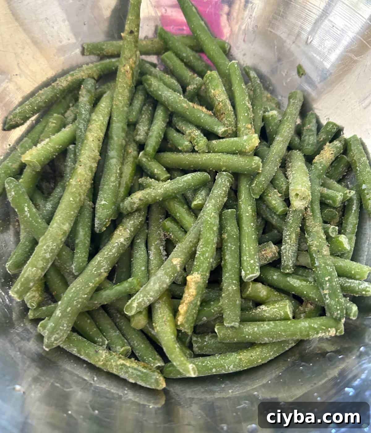Frozen green beans tossed in seasoning in bowl.