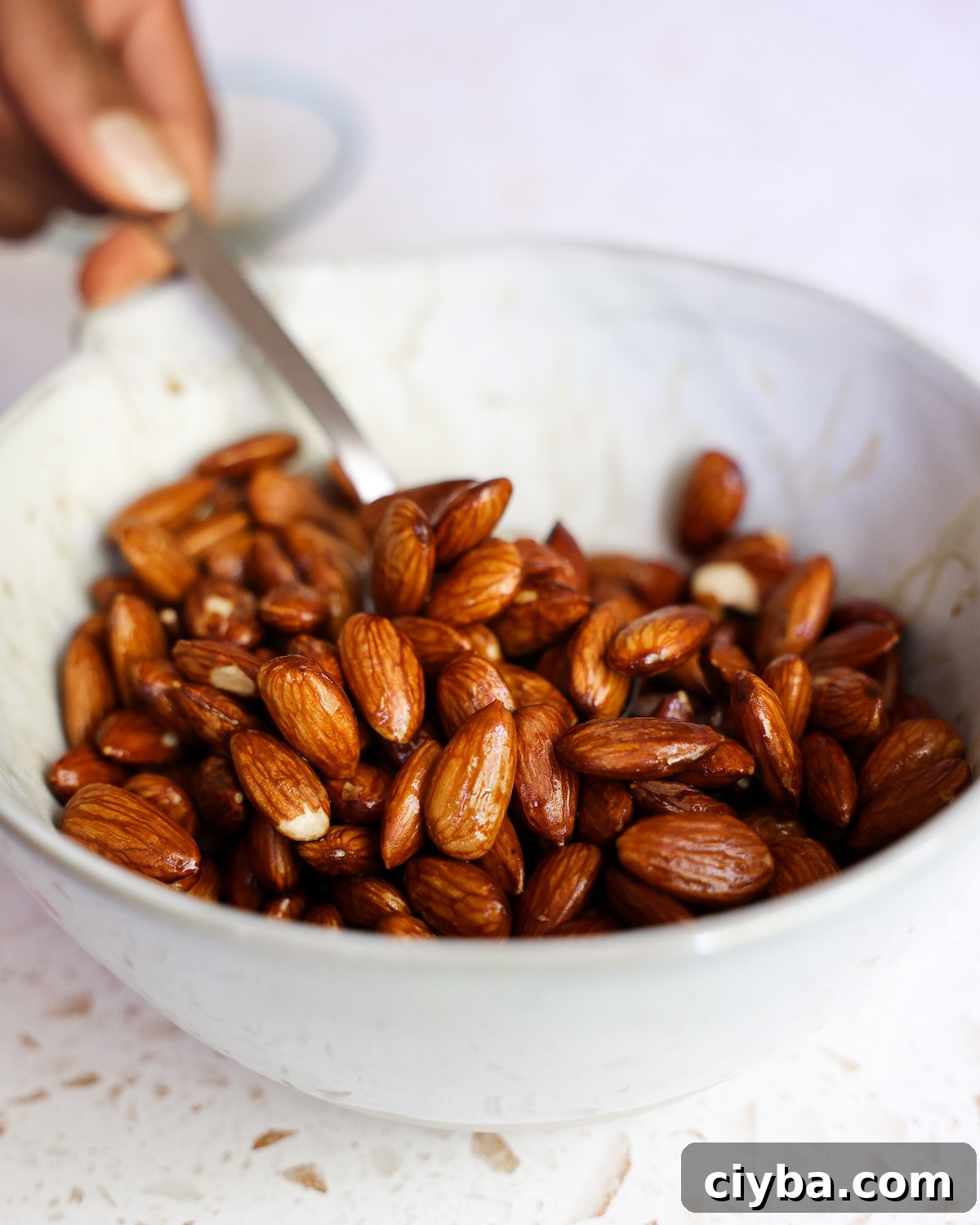 Stirring almonds with tamari in a white bowl before scooping out to drain.