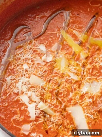 Red pot of homemade canned tomato soup with parmesan and olive oil drizzled on top.