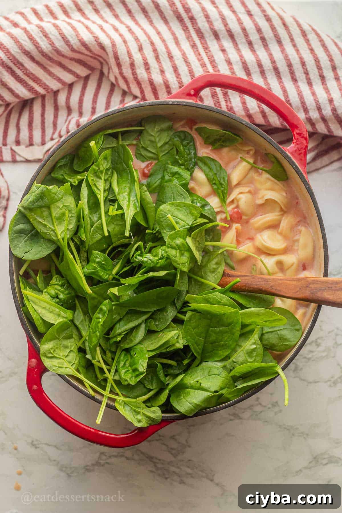 Spinach in soup pot with wooden spoon and tortellini.