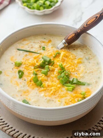 Bowl of cooked cauliflower leek potato soup on plate with wooden spoon.