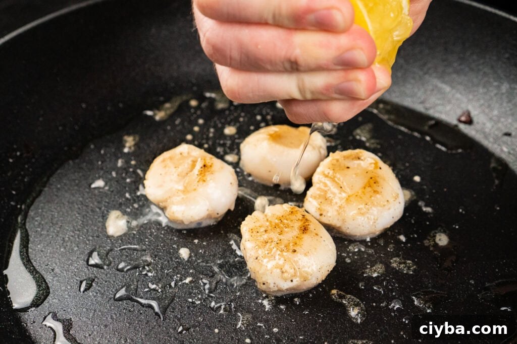 Squeezing lemon juice over four scallops cooking in a pan