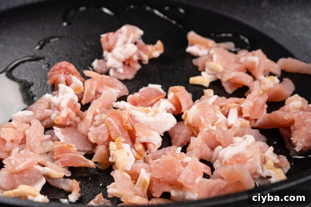 Chopped up bacon being fried in a pan
