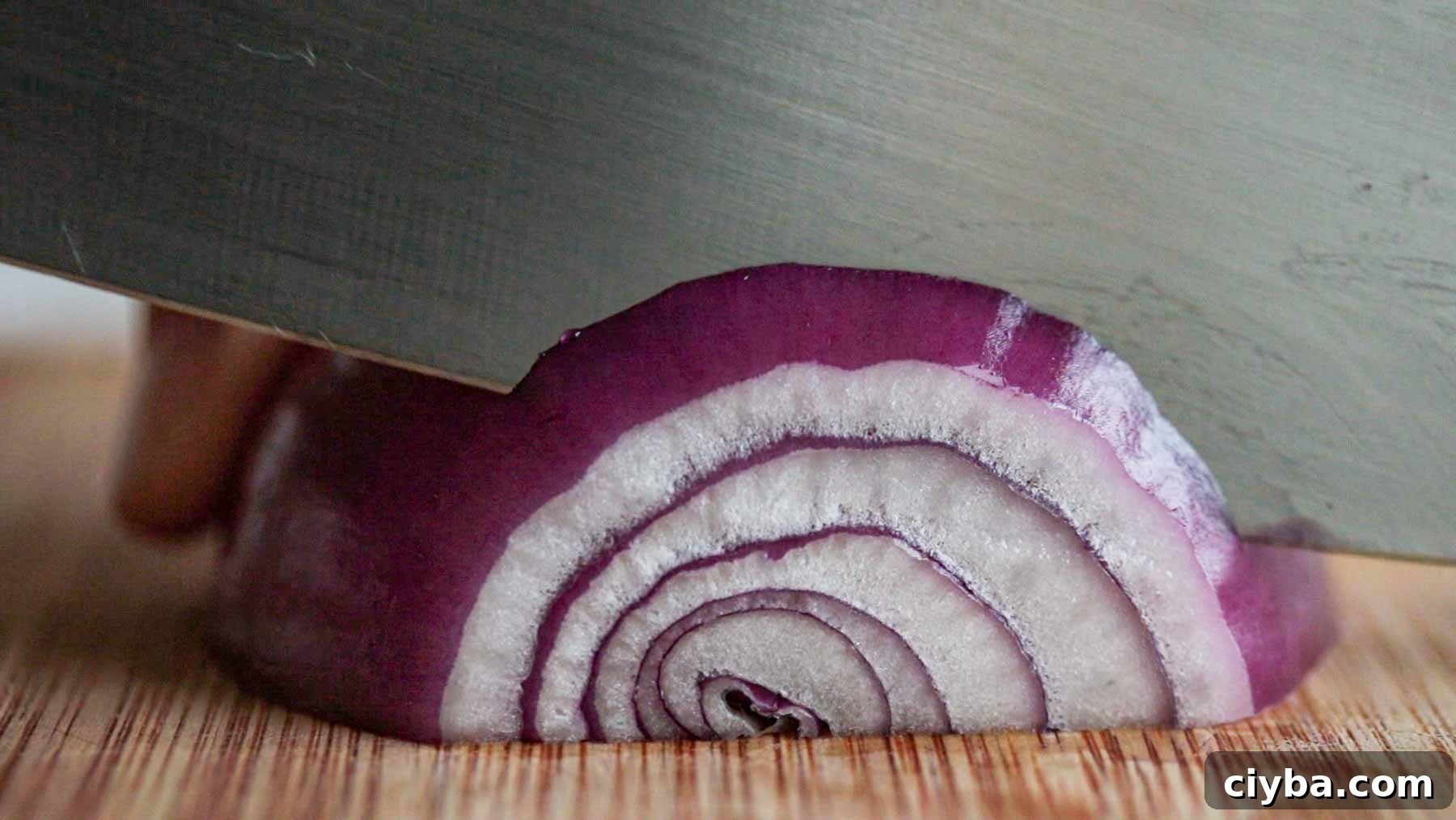 Knife slicing a red onion into half-moon slices.