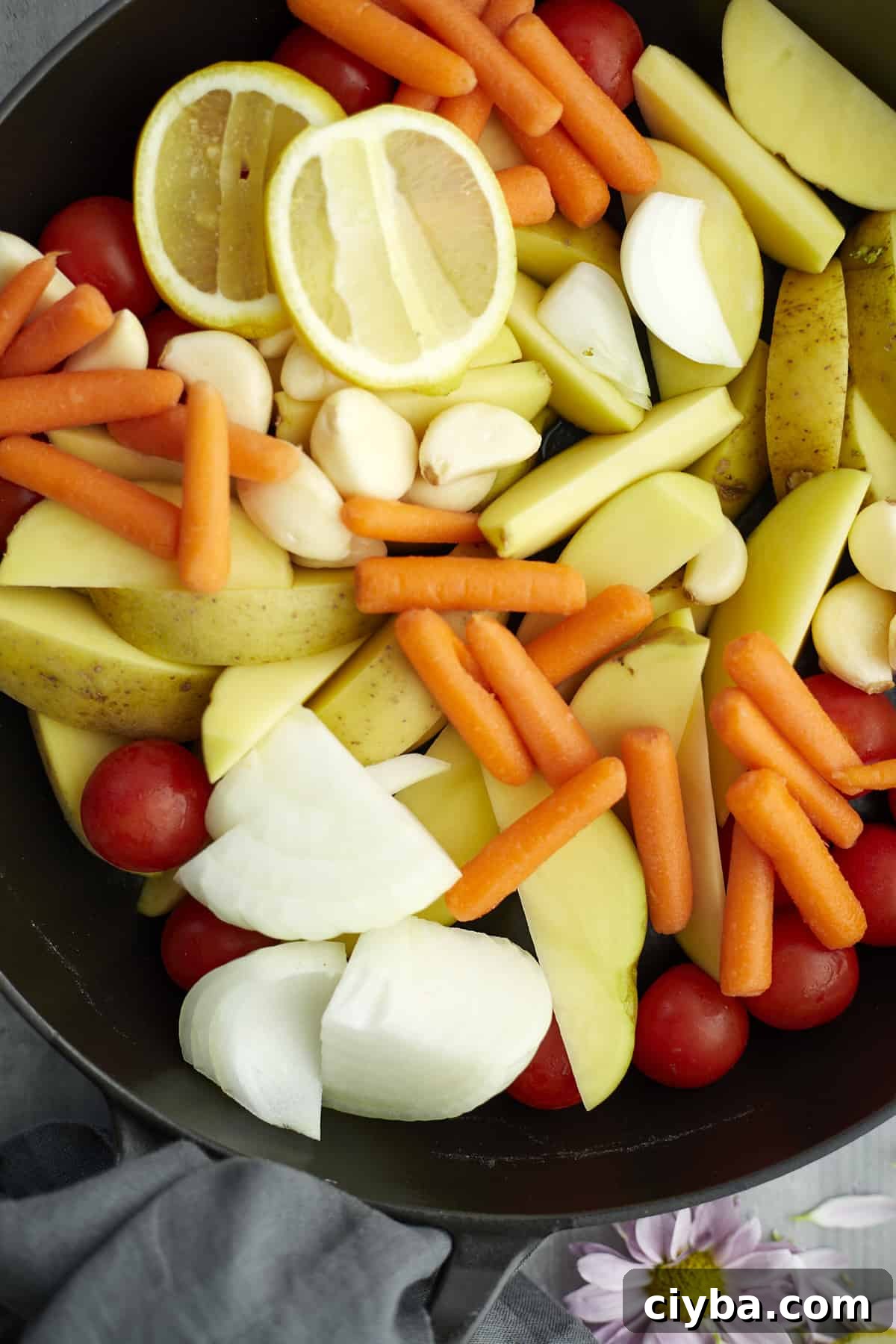 overhead potatoes, carrots, onions, tomatoes, garlic, and lemon in a pan