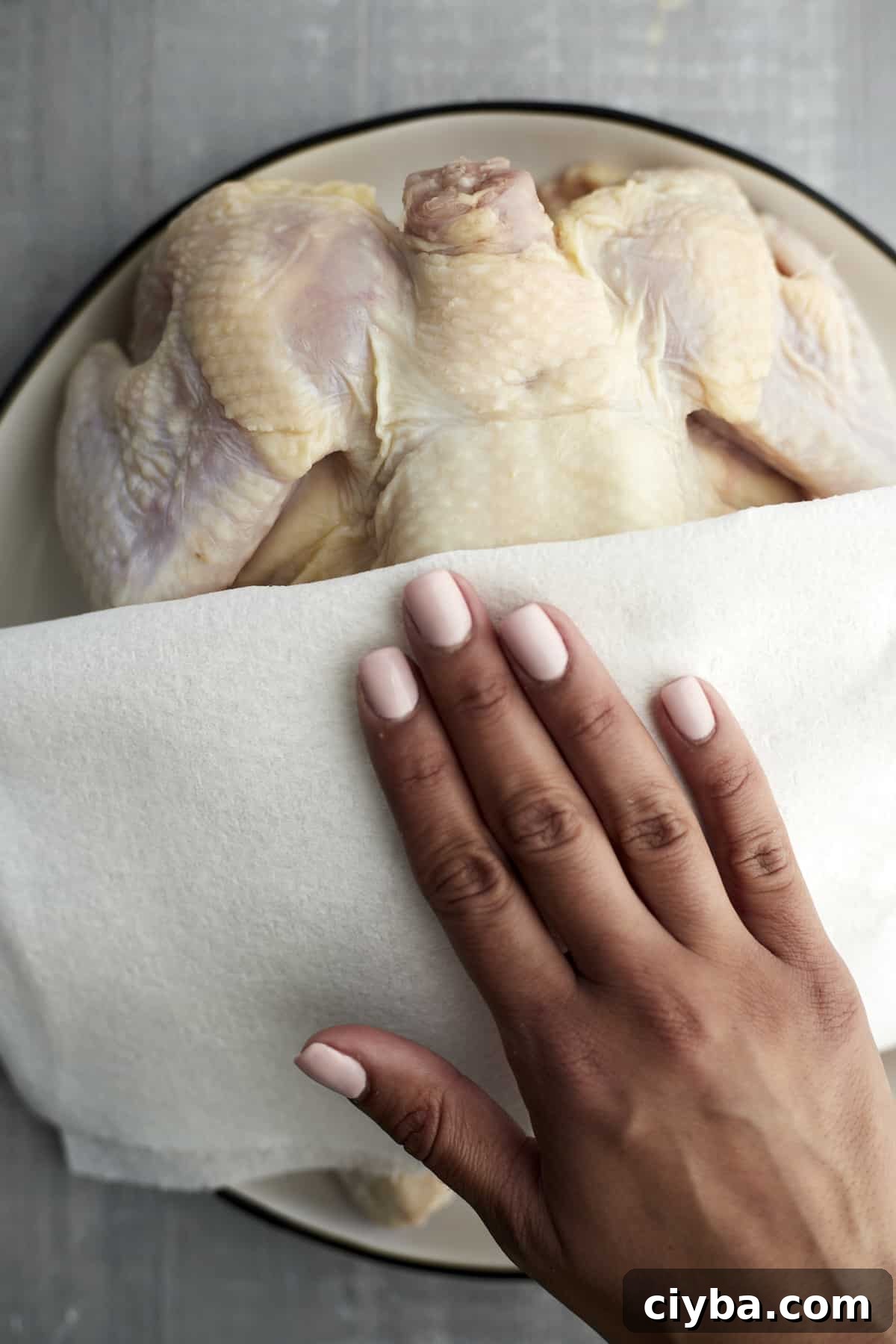 a hand using a paper towel to pat a whole raw chicken dry