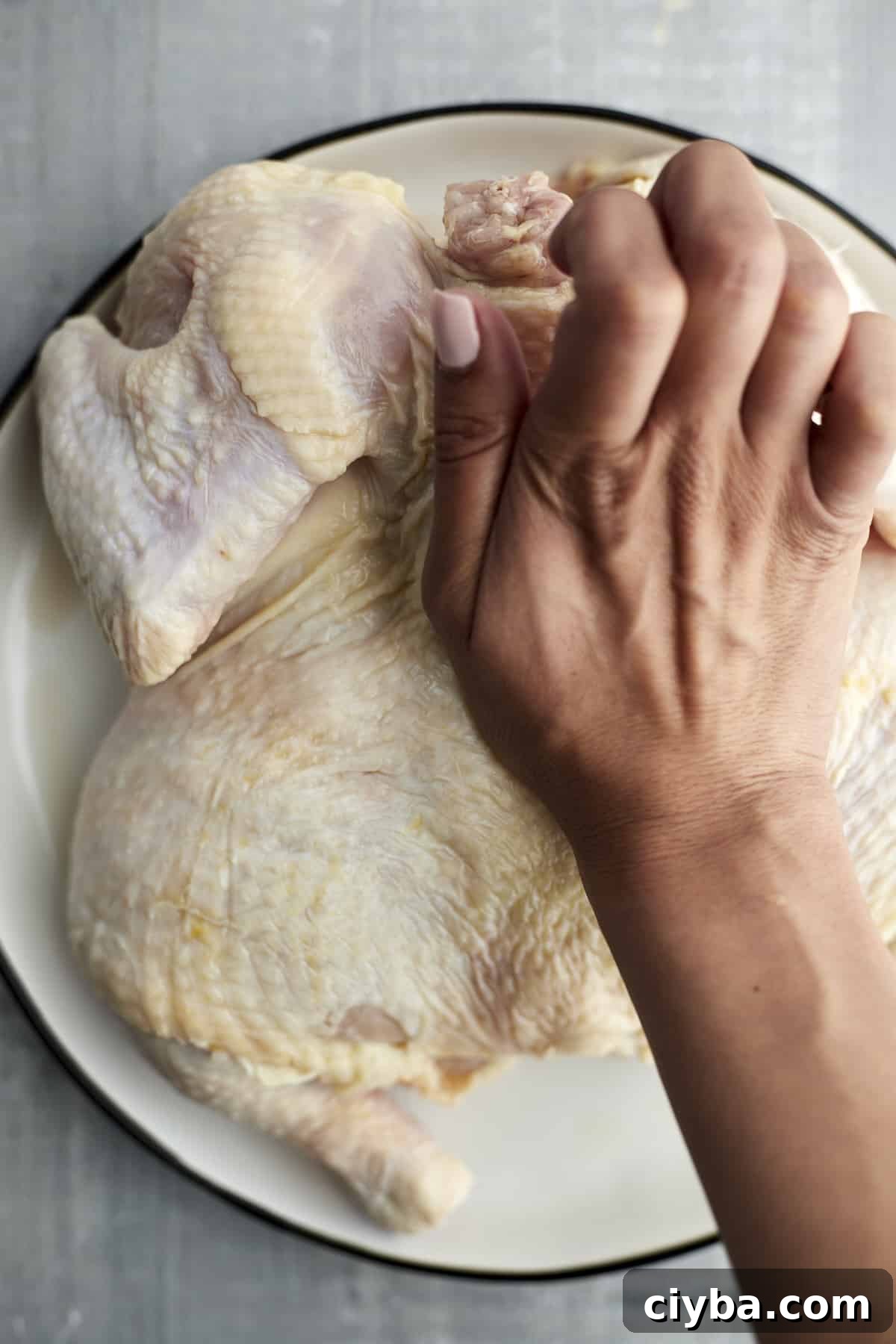 a hand butterflying a raw whole chicken