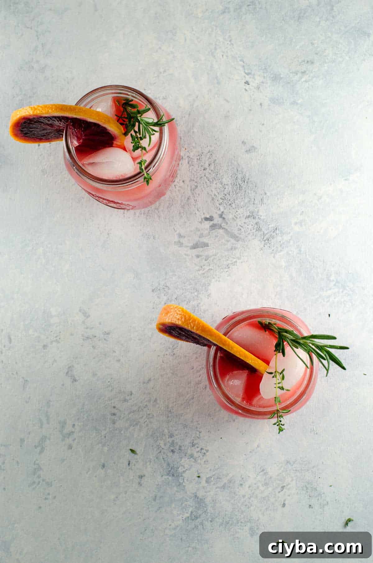 two blood orange cocktails in mason jars, each garnished with a rosemary sprig and a blood orange wheel