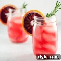 two blood orange cocktails in mason jars, each garnished with a rosemary sprig and a blood orange wheel