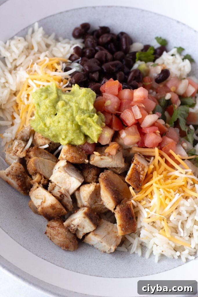 close up of a grilled chicken burrito bowl with white rice, pico de gallo, black beans, guacamole, and shredded cheese.