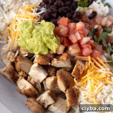 close up of a grilled chicken burrito bowl with white rice, pico de gallo, black beans, guacamole, and shredded cheese.