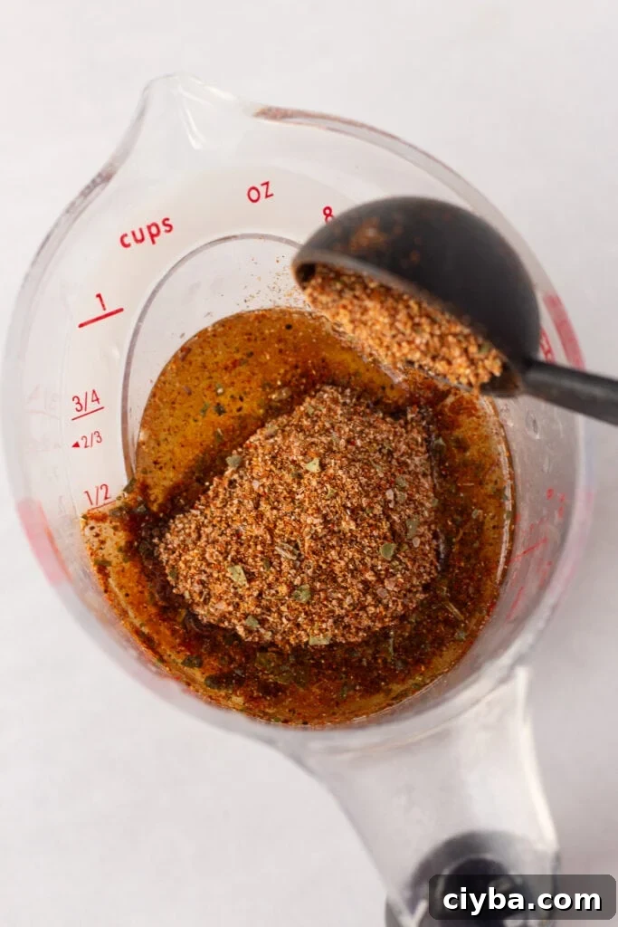 Close up of spices being poured into a liquid measuring cup of oil and lime juice.