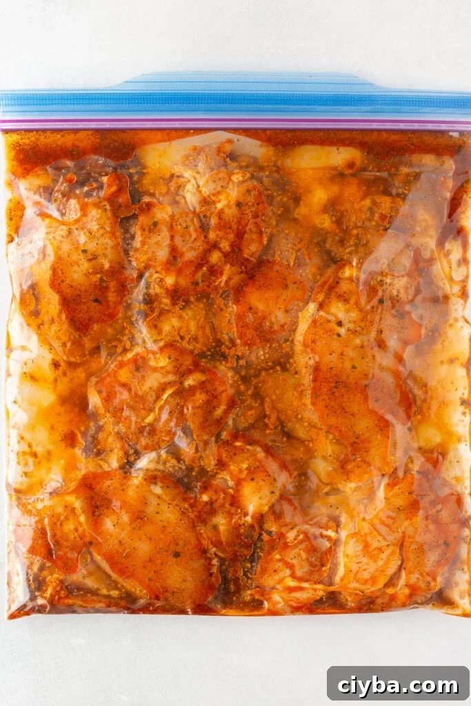 Top down shot of boneless skinless chicken thighs covered in a red marinade in a gallon sized plastic ziploc bag.