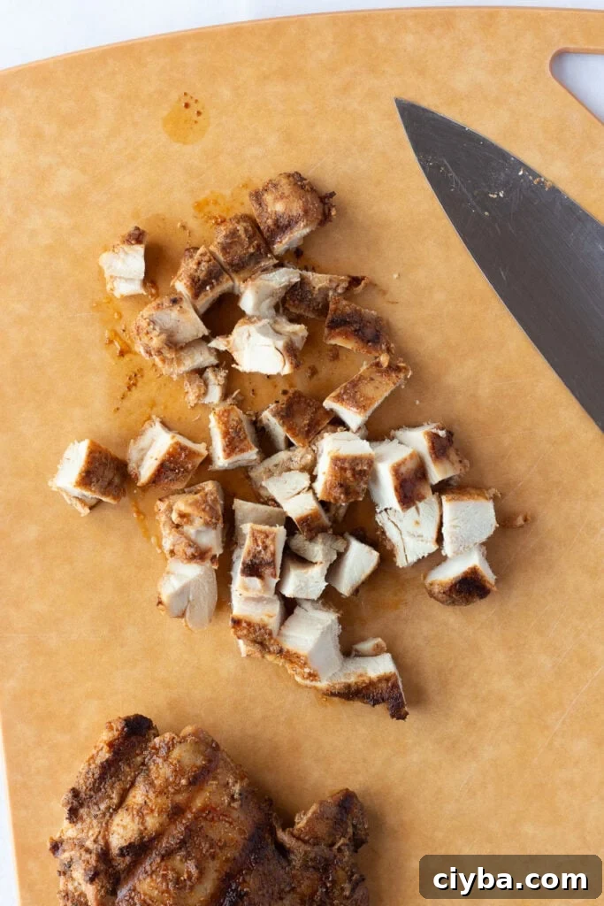 Top down shot of grilled chicken thighs being chopped on a wood cutting board.