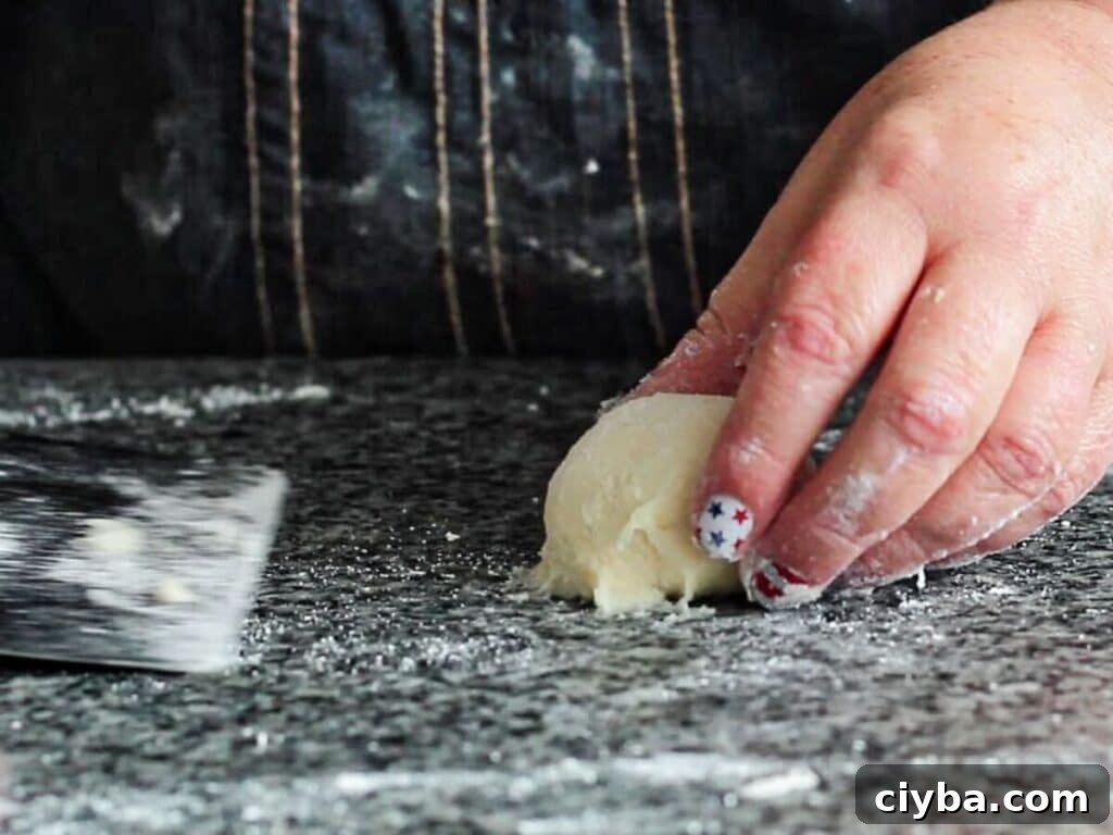 using bench scraper to scrape ball of dough from counter.