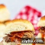 kahlua pork sliders on wooden cutting board with red checked napkin in the background.