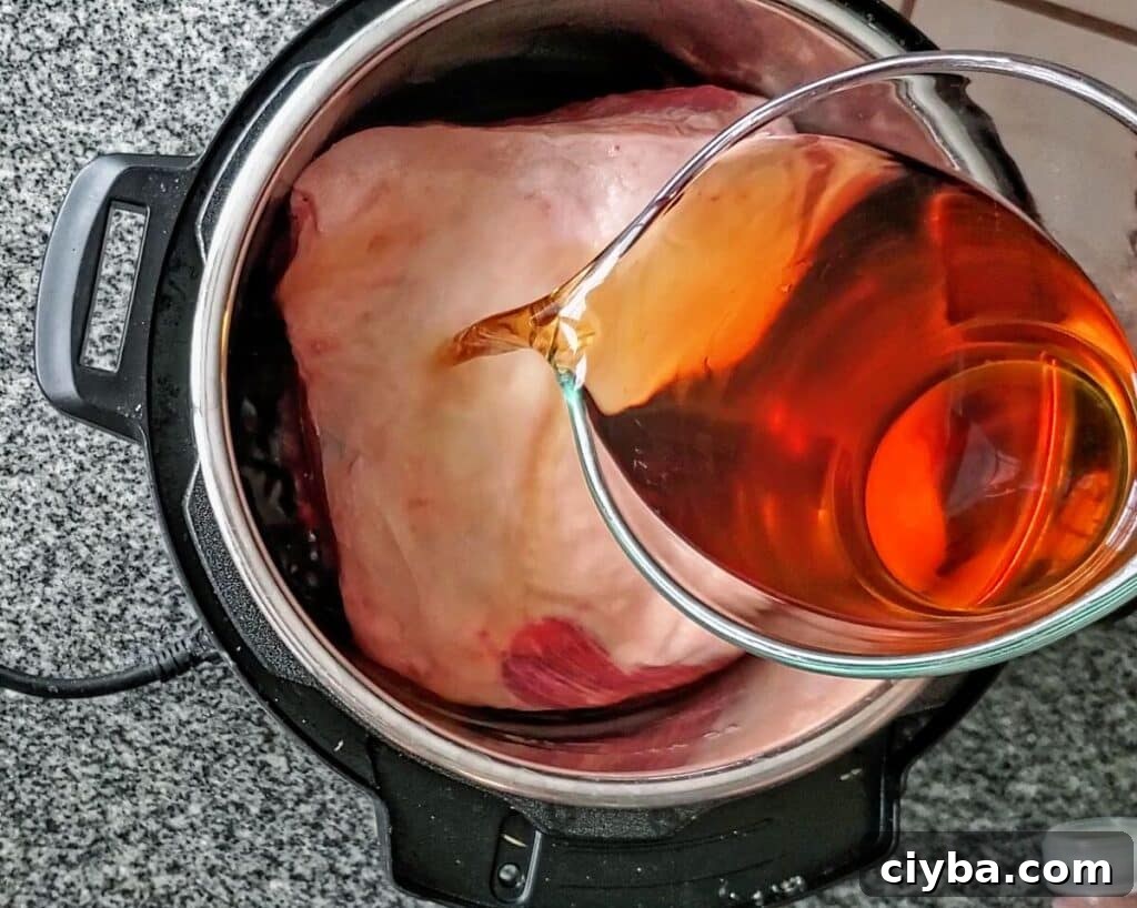 pouring apple cider and liquid smoke over pork shoulder in instant pot.