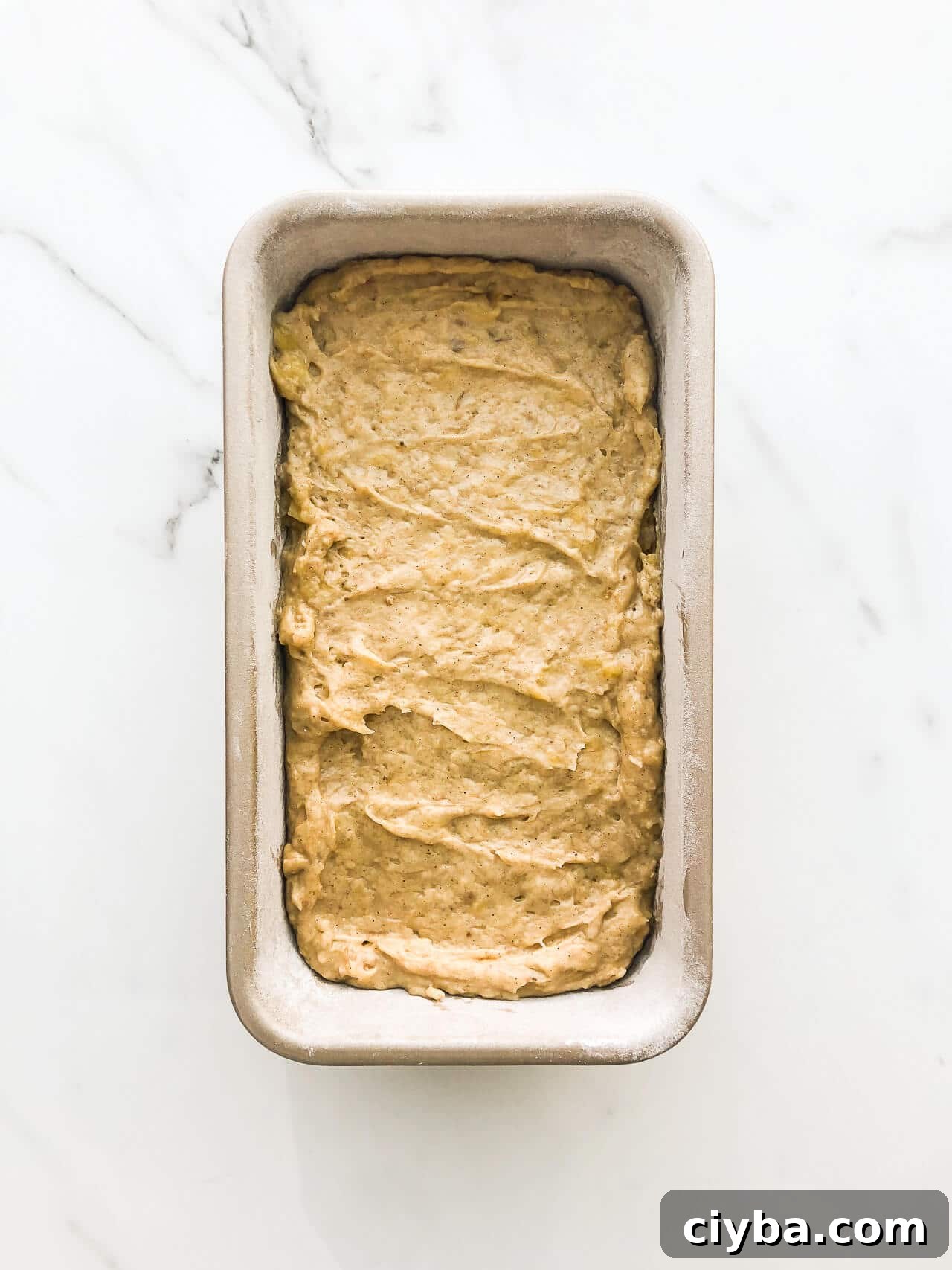 Banana bread batter in a loaf cake pan on marble surface