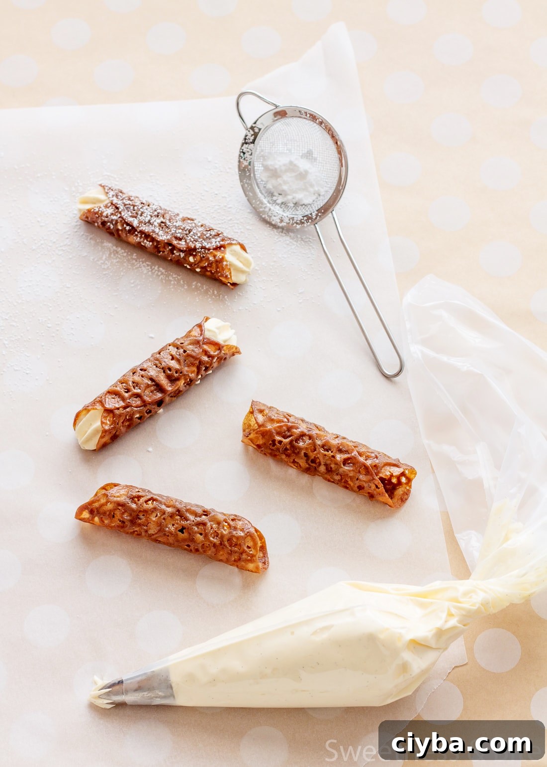 Four brandy snaps on a piece of baking paper, with a small sieve holding icing sugar.