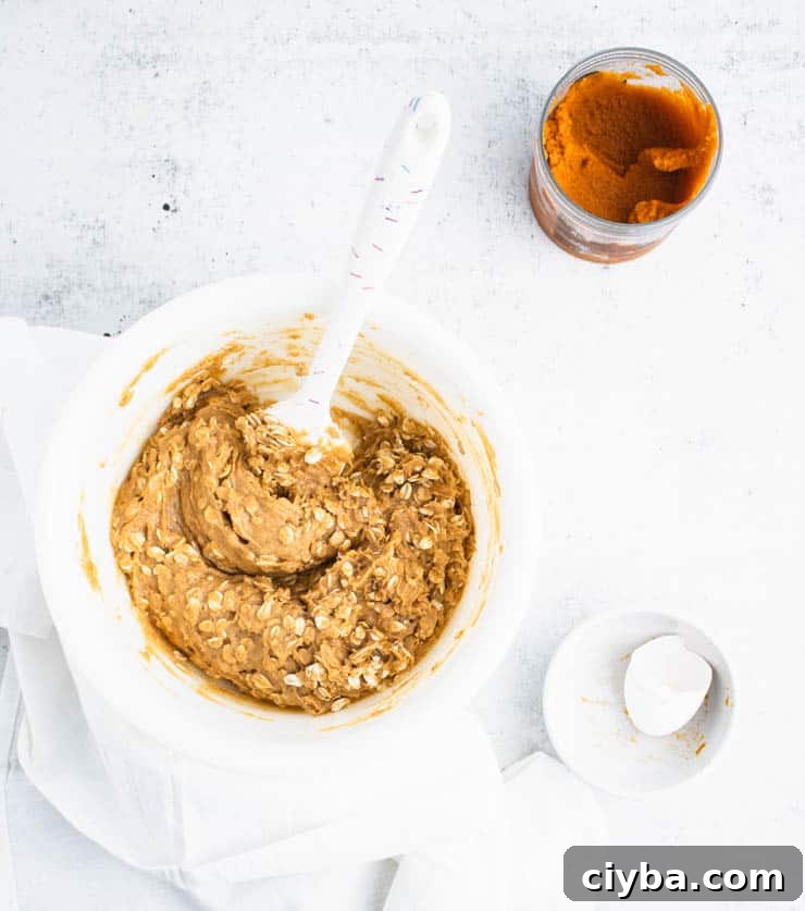 Pumpkin Oatmeal Cookies with Brown Butter Glaze 3 pumpkin cookie batter with visible bits of rolled oats in a white bowl next to a bowl with egg shells and a container of pumpkin puree.