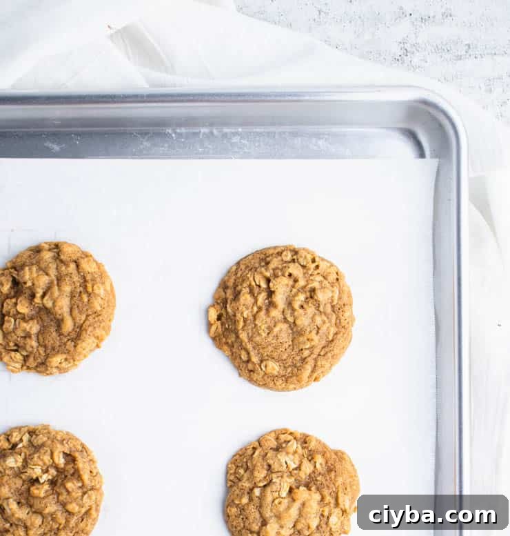 Pumpkin Oatmeal Cookies with Brown Butter Glaze 4 baked pumpkin oatmeal cookies on parchment paper on a silver baking sheet.