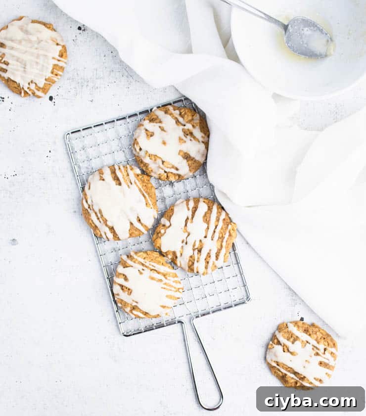 Pumpkin Oatmeal Cookies with Brown Butter Glaze 6 brown butter iced pumpkin cookies on a small silver cooling rack next to a piece of white linen and a bowl.