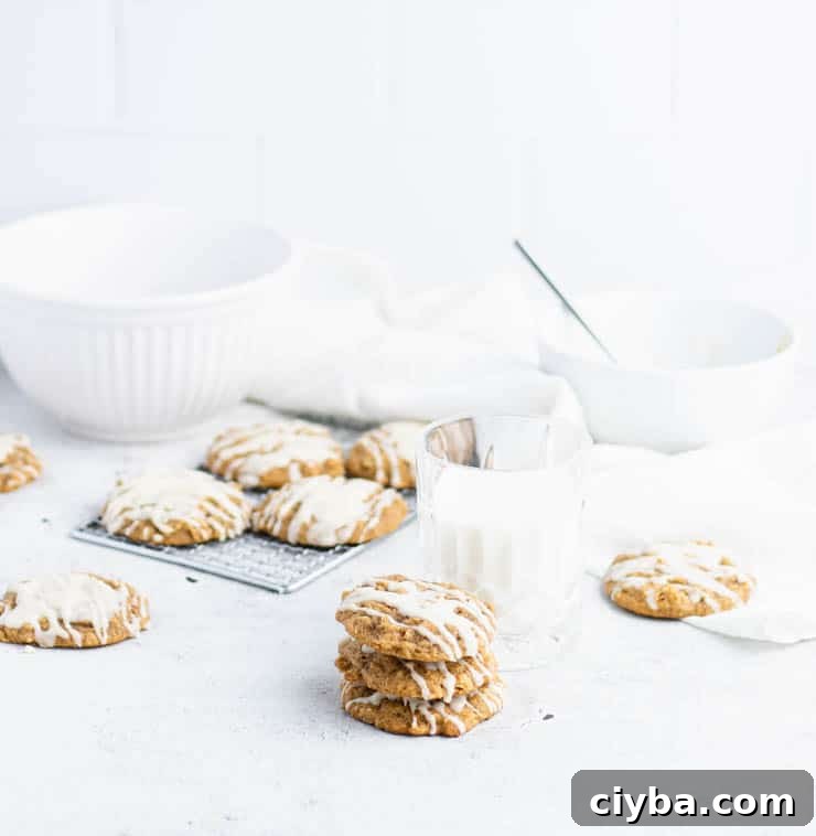 Pumpkin Oatmeal Cookies with Brown Butter Glaze 7 Iced pumpkin oatmeal cookies stacked in front of a cooling rack of cookies, and white bowls.