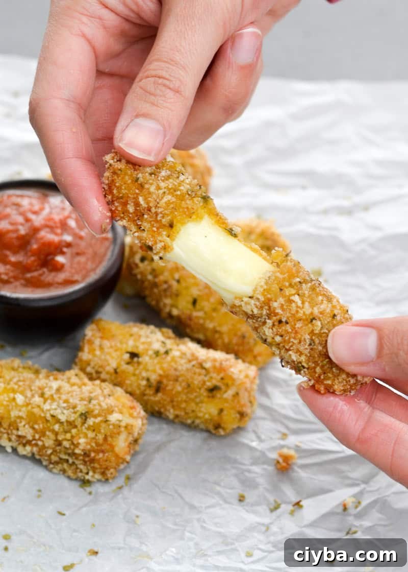 a hand pulling apart a gluten free cheese stick to show the perfect gooey, melty cheese