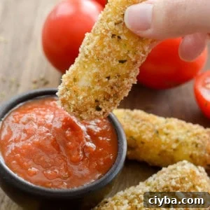 a hand dipping a crispy homemade mozzarella stick into marinara sauce