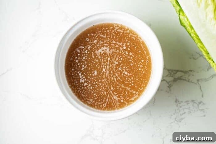 small bowl of bacon grease dressing for wilted lettuce salad next to a head of romaine lettuce