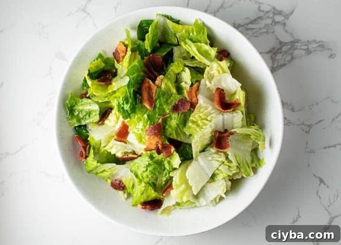 closeup of white bowl containing wilted lettuce salad with bacon