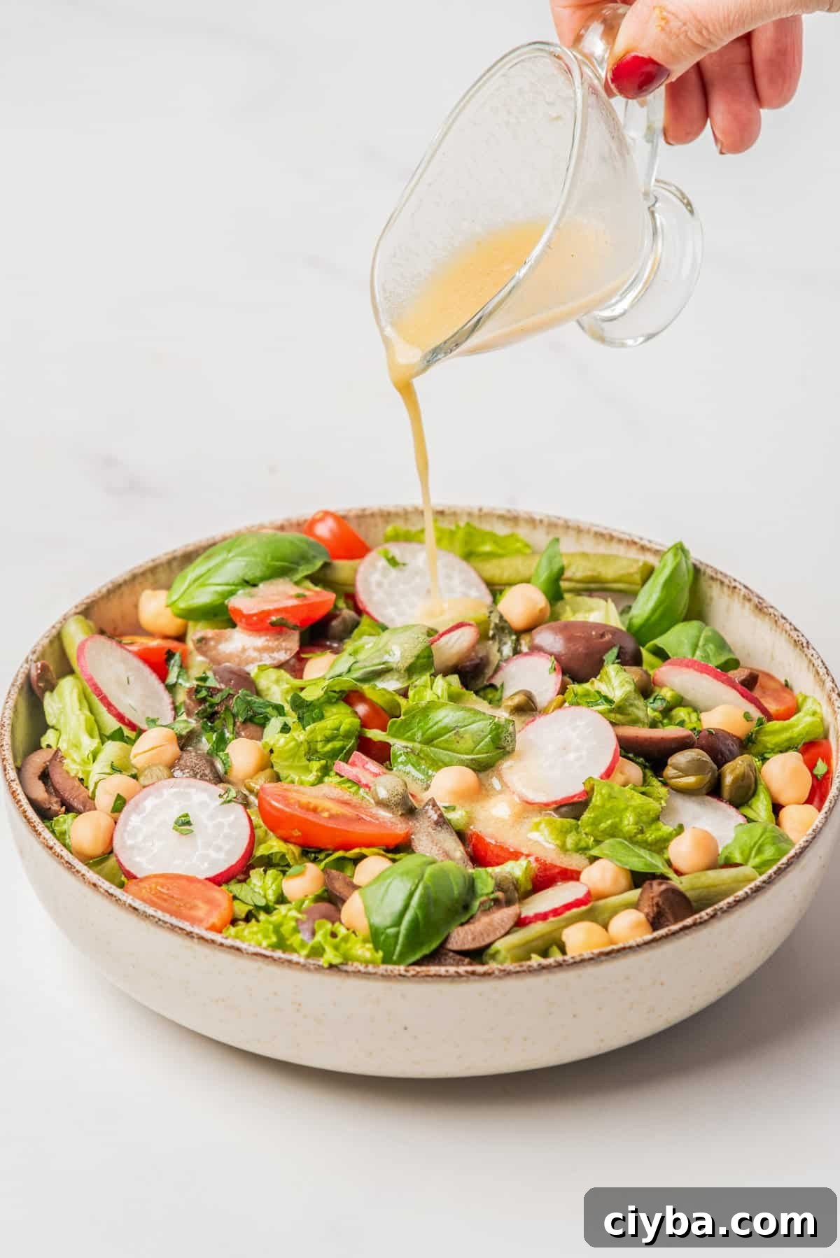 Vegan Niçoise Salad Recipe with Crispy Tofu and Olives 7 An image of vegan nicoise salad served on a big bowl while being drizzled by champagne vinaigrette.