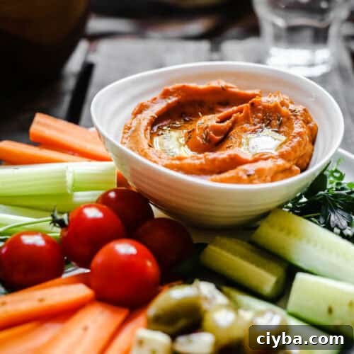 A bowl of Cumin Whipped Butternut Squash and Red Pepper Dip on a plate of crudites