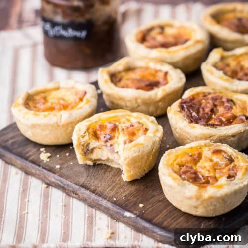 Mini Quiche on a wooden board. One with bite taken out showing meaty creamy inside.
