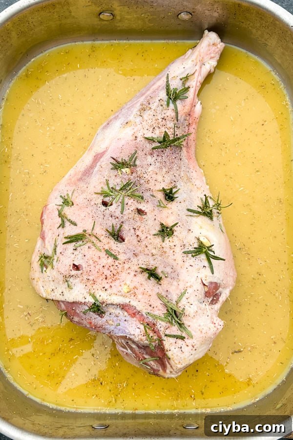 leg of lamb studded with rosemary and garlic in a tray with lemon and broth