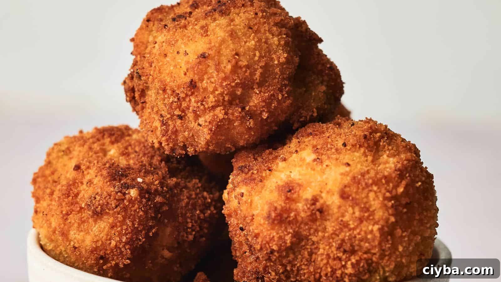 A bowl of golden-brown, crispy fried arancini served in a white dish on a plain background.