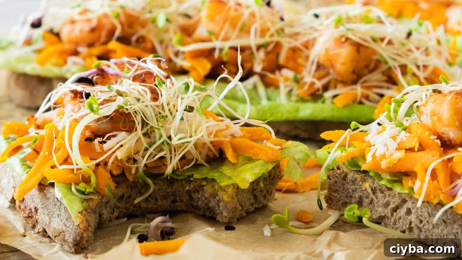 Close-up of open-faced sandwiches topped with avocado, shredded carrot, microgreens, and pieces of cooked salmon on whole-grain bread.
