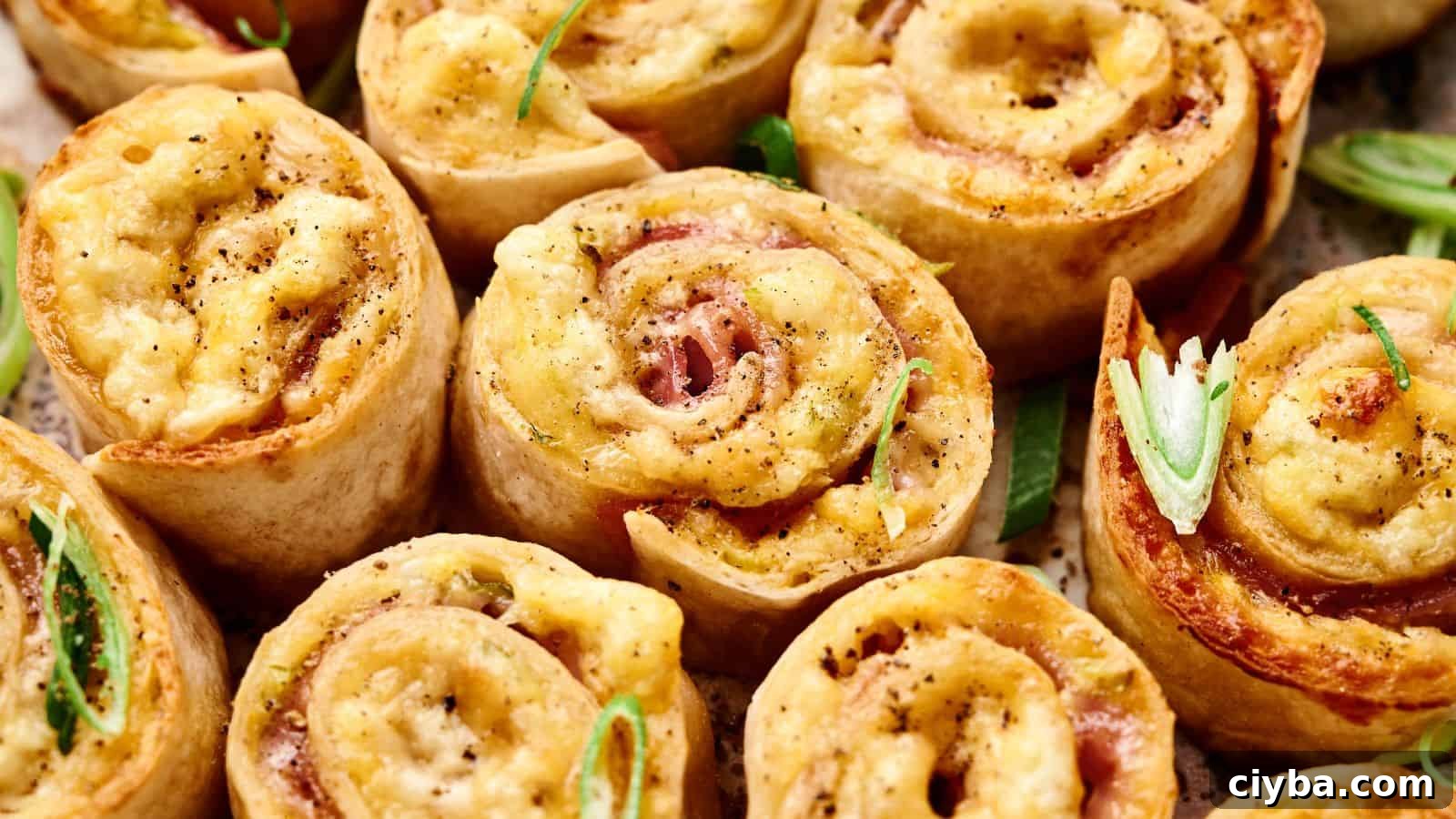 Close-up of baked pinwheel appetizers filled with cheese and ham, topped with black pepper and garnished with sliced green onions.