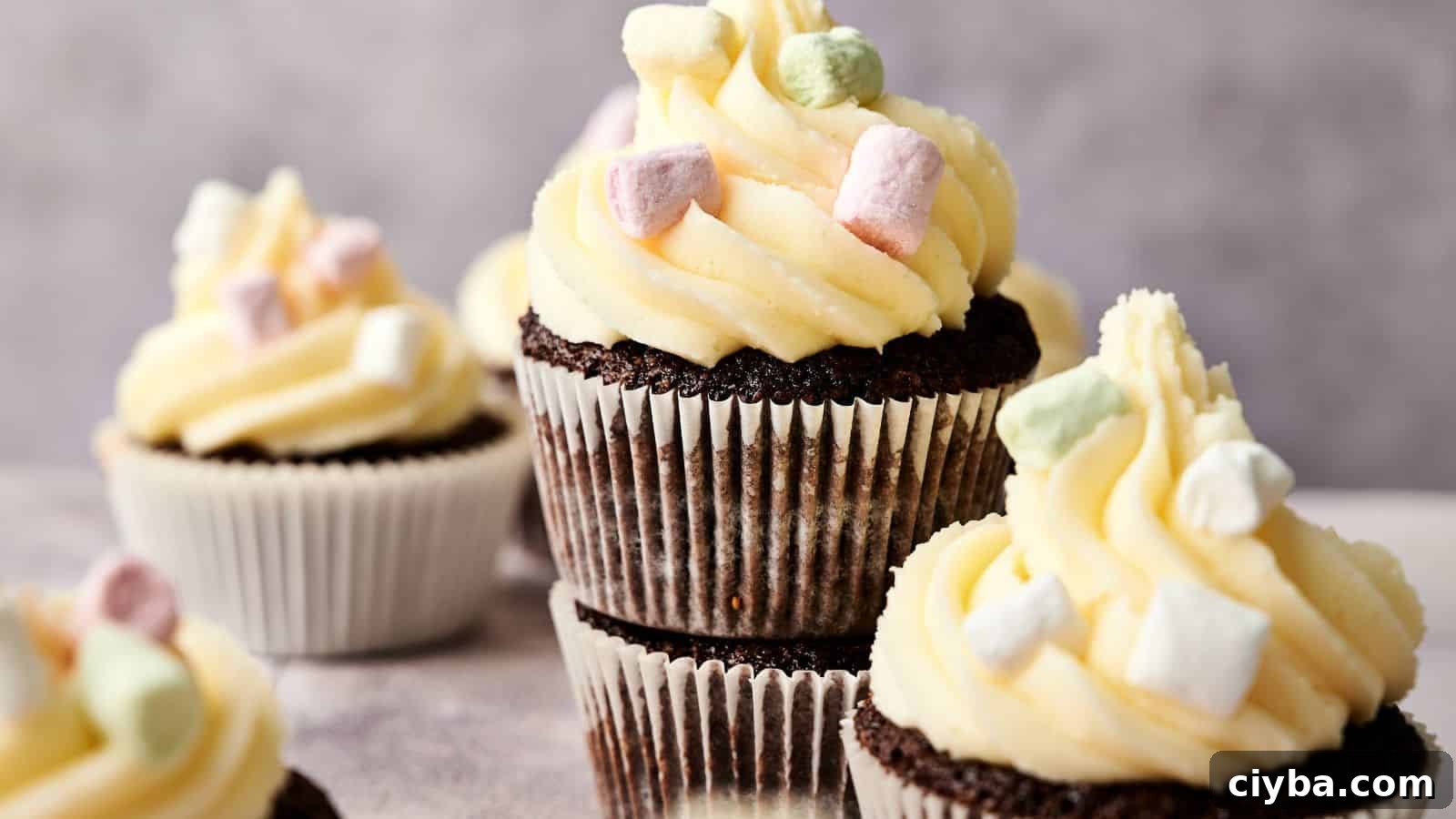 Chocolate cupcakes with white frosting and small pastel-colored marshmallows on top, arranged in a group against a neutral background.
