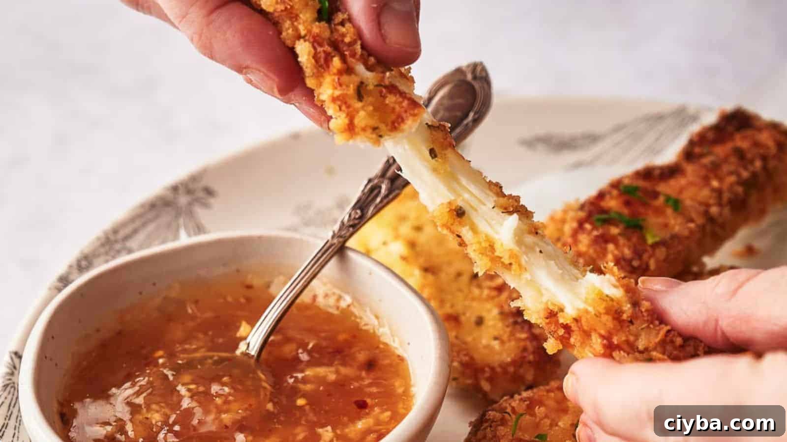 Someone pulling a mozzarella stick apart and showing the stretchy cheese.
