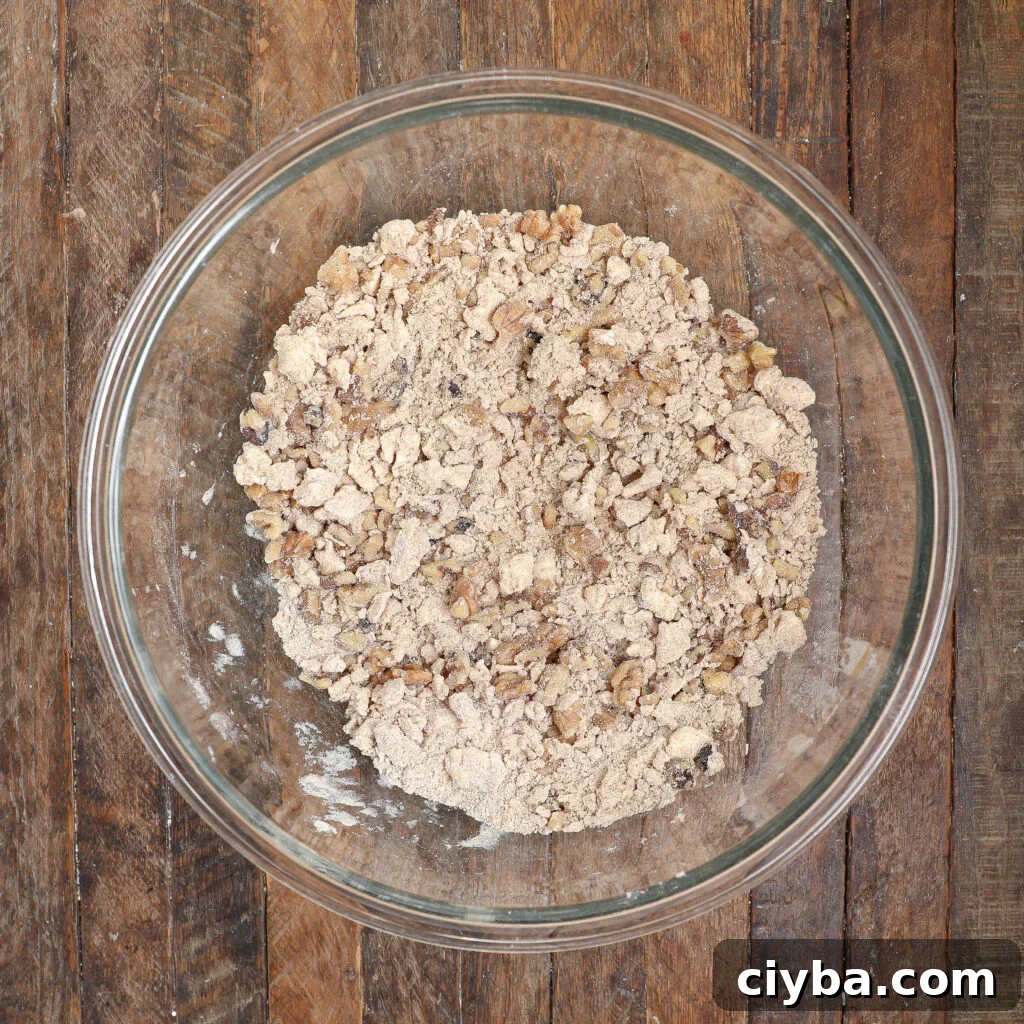 Cream Cheese Apple Coffee Cake Recipe for Fall Baking 5 A clear glass bowl filled with the crumbly mixture for an Apple Coffee Cake with Cream Cheese sits on a rustic wooden surface.