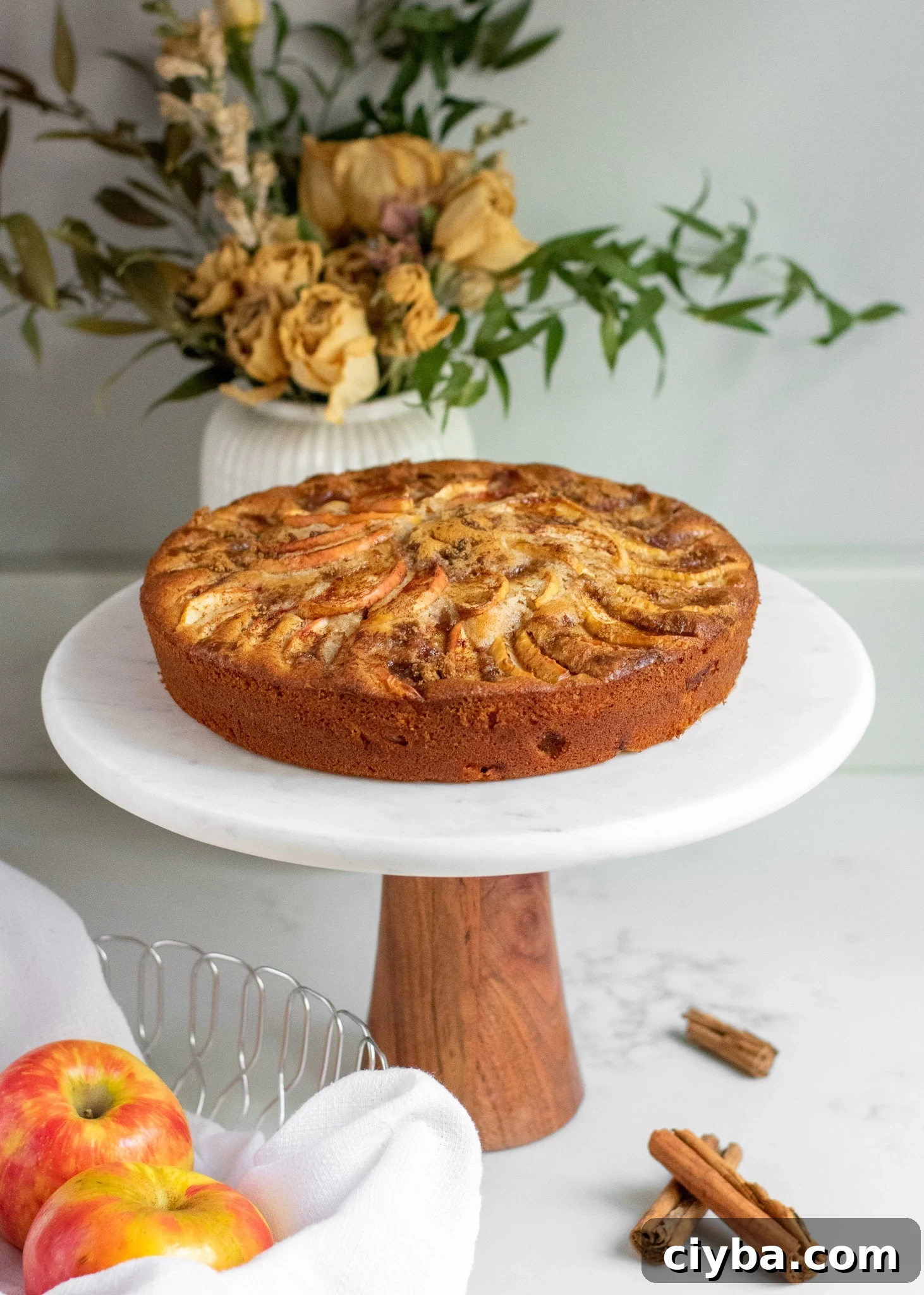 Apple cake on a cake stand topped with cinnamon and brown sugar.