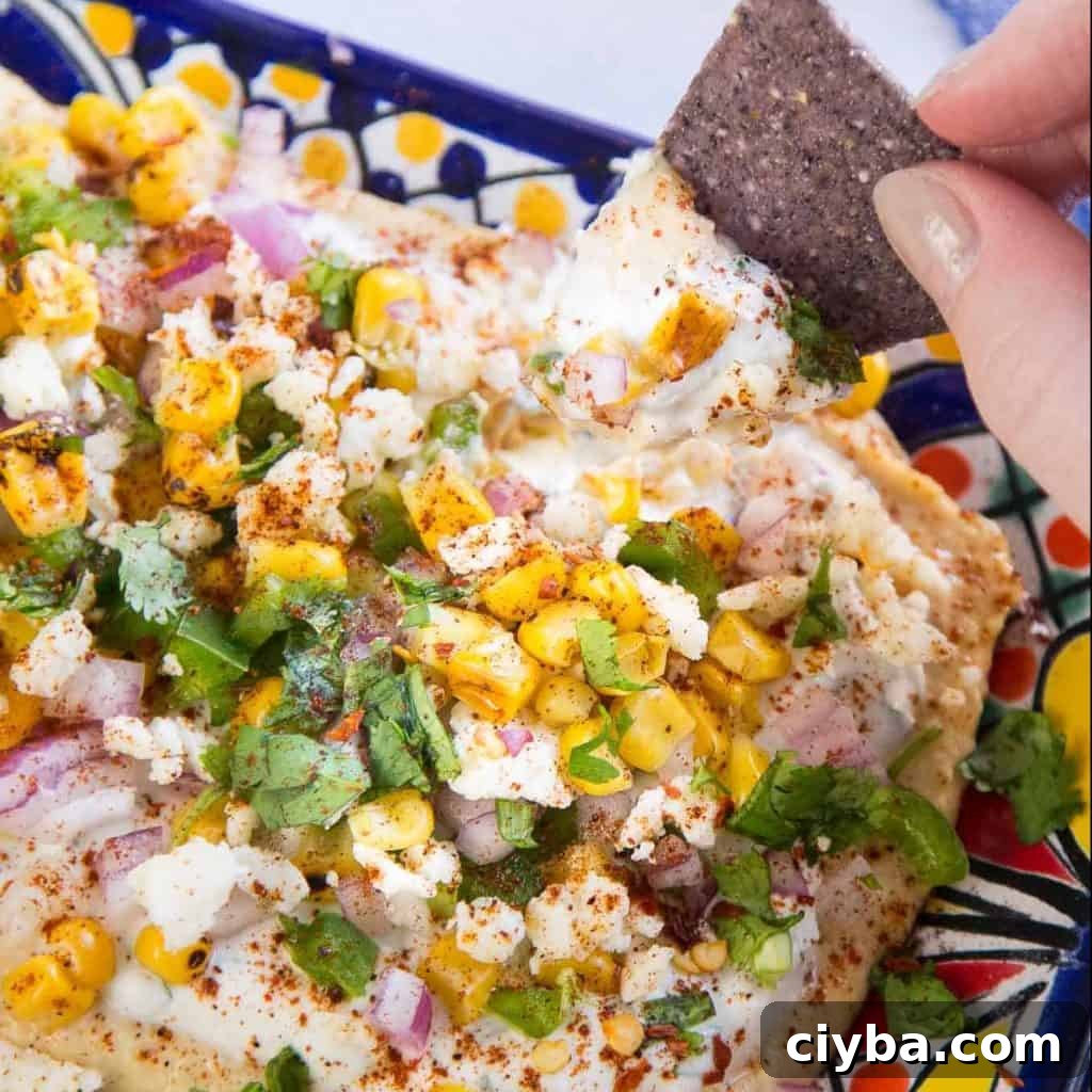 Creamy Mexican Street Corn Dip Recipe for Parties 2 Tortilla chip scooping up mexican street corn dip from a colorful platter.