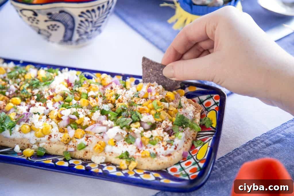 Creamy Mexican Street Corn Dip Recipe for Parties 4 hand dipping a blue corn tortilla chip into mexican street corn dip.