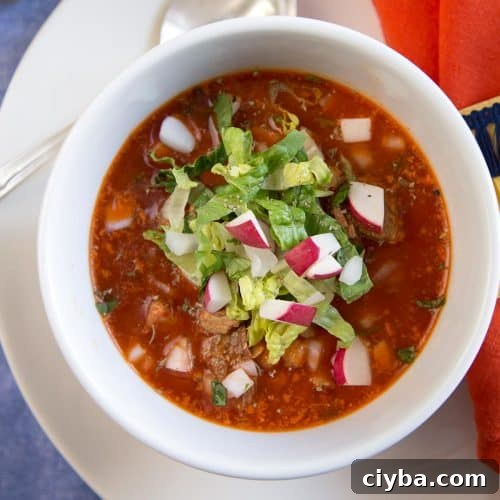 red pozole in a white bowl, topped with chopped romaine and chopped radishes.